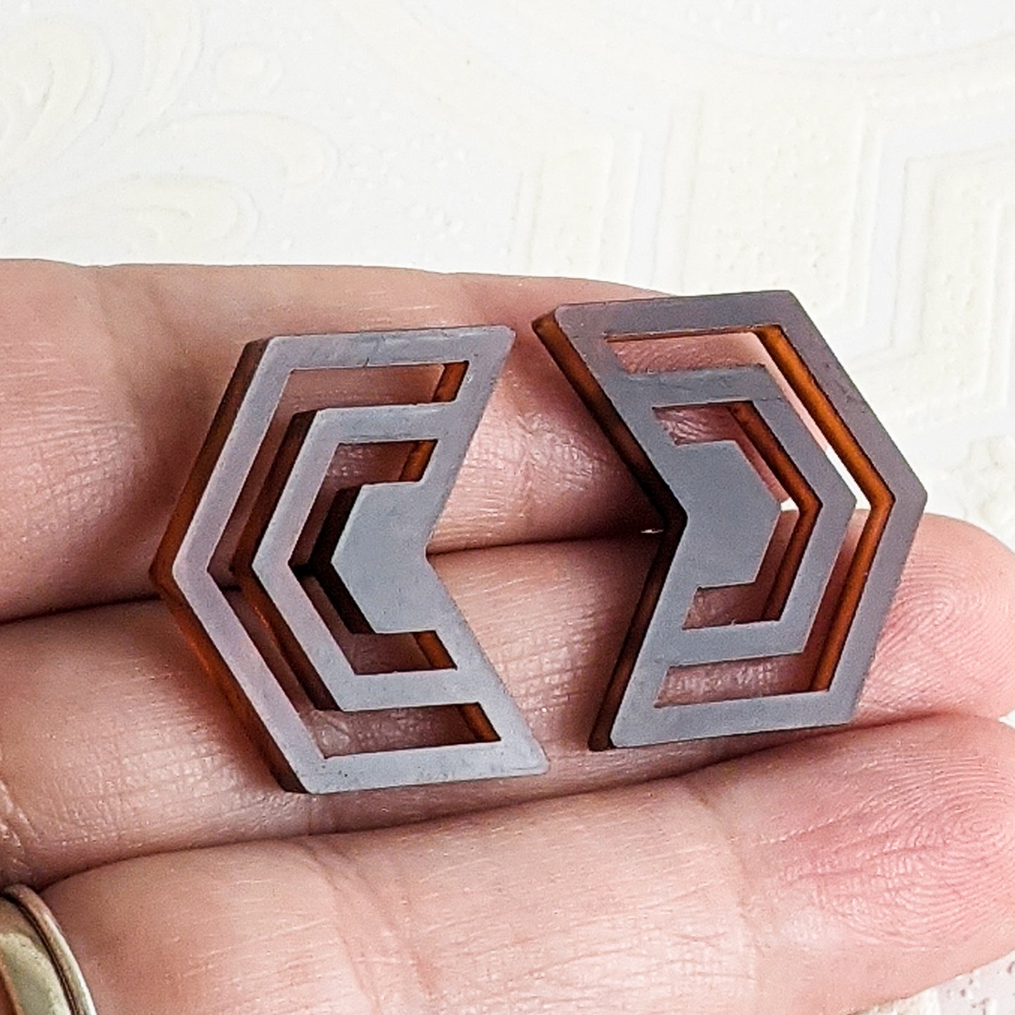 Warm translucent brown and gold tortoiseshell acrylic cut into Irregular Radiating Hexagon Earrings held, showing that the earrings are less than the height of two fingers.  