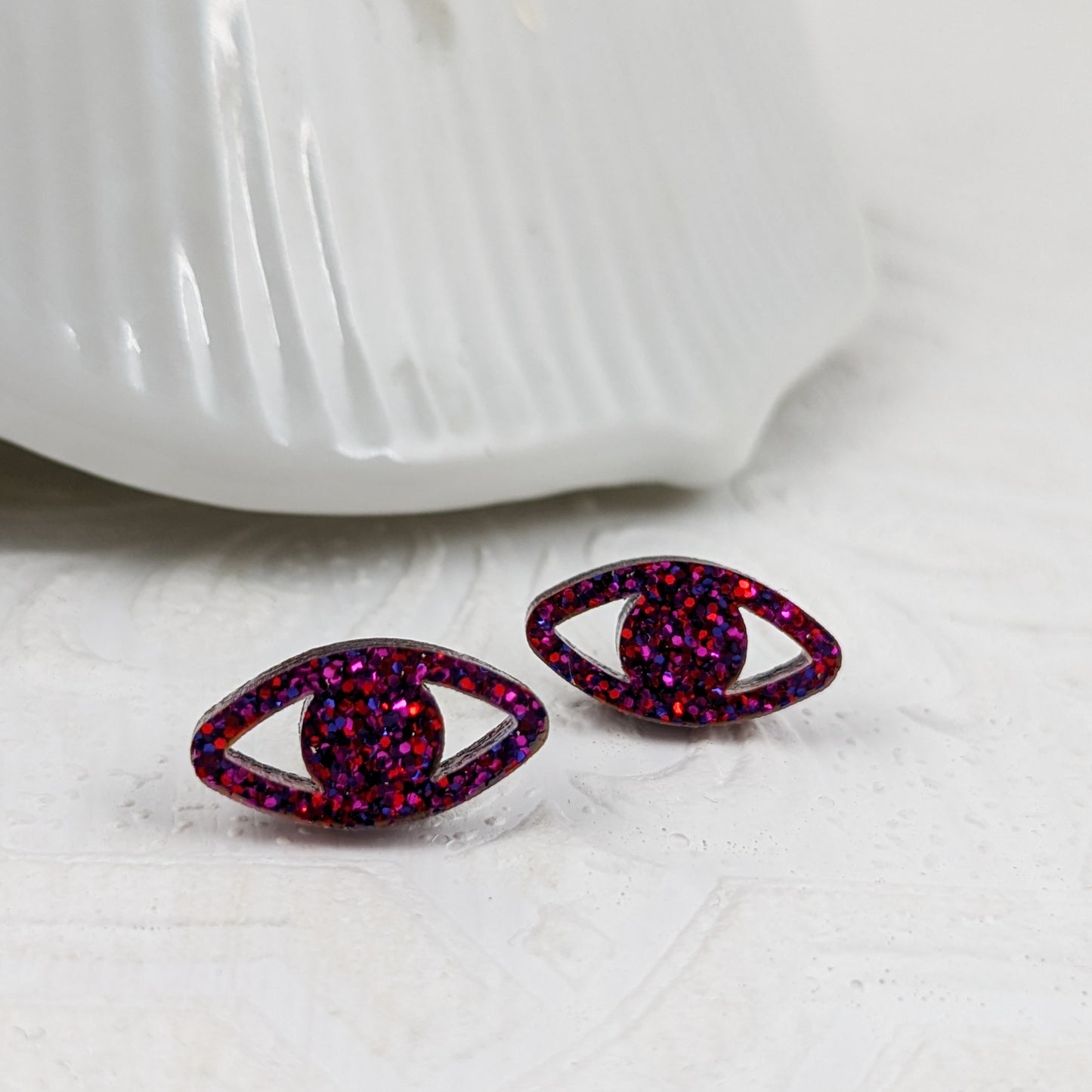 Eye shaped stud earrings made with ruby sparkle acrylic and stainless steel posts, white background