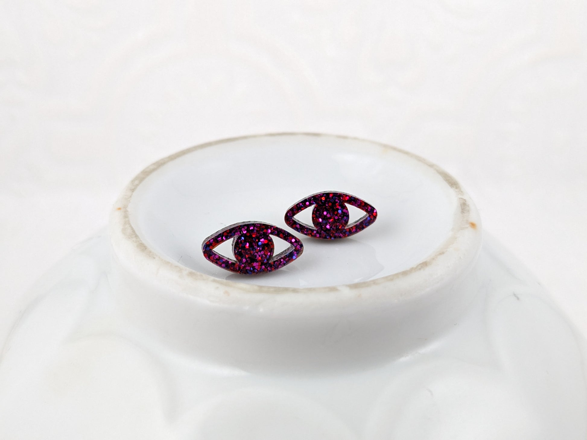 Eye shaped stud earrings made with ruby sparkle acrylic and stainless steel posts on vintage white dish